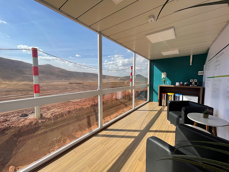 Interior de container humanizado com piso amadeirado, poltronas e vista panorâmica